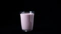 Strawberry milkshake isolated on black background. Frame. Transparent glass filled with pink milkshake stands on black