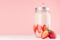 Strawberry milkshake with slices ripe berry in jar on gentle pastel pink and white background, closeup, copy space.