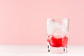 Strawberry red cocktail in shot glass with ice cubes on white wood table and pastel pink wall, copy space. Royalty Free Stock Photo