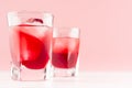 Strawberry red cocktails in two shot glasses with ice cubes closeup on white wood table and pastel pink wall, copy space. Royalty Free Stock Photo