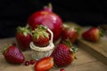 Strawberry in a small basketball on wooden board with fruit cream pomegranate and other strawberries in a dark background