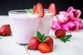 Strawberry smoothie with fresh berries and pink flowers on white wood table and dark background. Fresh milkshake Royalty Free Stock Photo