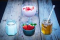 Strawberry smoothie ingredients: fresh strwawberries in a bowl, honey and yogurt in jars