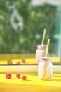 Strawberry smoothie in a jar with drinking straws on a windowsill on a bright sunny day. ripe strawberries on a yellow background