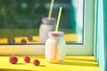 Strawberry smoothie in a jar with drinking straws on a windowsill on a bright sunny day. ripe strawberries on a yellow background