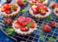 Strawberry tarts, small shortcrust tarts with the addition of cream cheese, fresh strawberries and mint on cooling tray on a dark Royalty Free Stock Photo