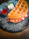 Strawberry waffles and whipped cream, garnished with mint leaves, served with strawberry sauce on a black plate Royalty Free Stock Photo