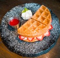 Strawberry waffles and whipped cream, garnished with mint leaves, served with strawberry sauce on a black plate Royalty Free Stock Photo