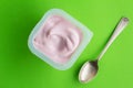 Strawberry yogurt cup on bright green background with small silver spoon