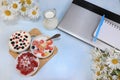 Strawberry yogurt, milk and ripe currant berries and strawberries next to a closed computer on a light background