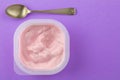 Strawberry yogurt in plastic cup isolated on lilac background - Top view photo of pink yoghurt and small silver spoon - text space Royalty Free Stock Photo