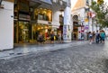 A stray dog stands on a sidewalk on Ermou Street, a busy shopping center in Athens Greece as tourists and locals shop and sightsee