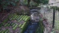 Stream channelled through a manmade wear made of concrete in brutalism style with hand rail railings.