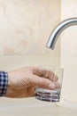 A stream of clean water pours from the tap into glass in kitchen.