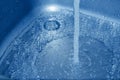 A stream of clean water running down the drain into the stainless steel sink in blue tones Royalty Free Stock Photo