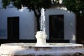 Stream of crystal clear water gushing out of stone fountain. In the background white walled house in mediterranean style in spain Royalty Free Stock Photo