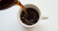 A stream of dark coffee is being poured into a white ceramic mug against a plain Royalty Free Stock Photo