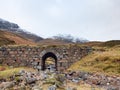 Stream and stony bridge in spring Hiigland mountains in Scotland. Snowy mountains in heavy clouds.