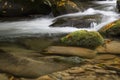 Stream with surface and submerged rocks with moss and fall leaves