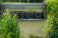 Stream with water flowing into a small weir under a bridge with a metal walkway, stuck branches Royalty Free Stock Photo