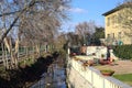 Stream of water next to a group of houses and bordered by bare trees on a sunny day in winter