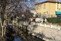 Stream of water next to a group of houses and bordered by bare trees on a sunny day in winter