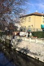 Stream of water next to a group of houses and bordered by bare trees on a sunny day in winter