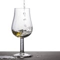 Stream of white wine is pouring into a glass on a white background