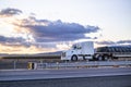 Streamline big rig white semi truck with long hood transporting covered and fastened by slings cargo on flat bed semi trailer