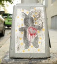 Street art bunny with a red dripping heart on the base of a sidewalk lamppost.