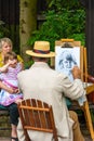 A street artist wearing straw boater hat. sketches small female child