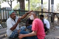 Street barber shaving a man using an open razor blade on a street in Kolkata