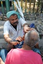 Street barber shaving a man using an open razor blade on a street in Kolkata