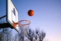 Street basketball ball falling into the hoop. Close up of orange ball above the hoop net with blue sky in the background. Concept Royalty Free Stock Photo