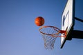 Street basketball ball falling into the hoop. Close up of orange ball above the hoop net with blue sky in the background. Concept Royalty Free Stock Photo