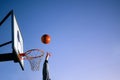 Street basketball ball player throwing ball into the hoop. Close up of hand, orange ball above the hoop net with blue sky in the Royalty Free Stock Photo