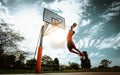 Street basketball player making a powerful slam dunk on the court - Athletic male training outdoor at sunset