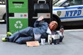 Street beggar wears a Trump mask and reading the book of Hillary Clinton What Happened.