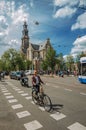 Street with blue sky, old brick church, people and cyclist passing by in Amsterdam.