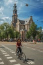 Street with blue sky, old brick church, people and cyclist passing by in Amsterdam.