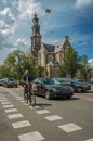 Street with blue sky, old brick church, people and cyclist passing by in Amsterdam.