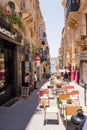 Street with building and umbrellas with cafe tables at restaurants in Valletta, Malta Royalty Free Stock Photo