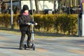 Street candid portrait of a sunlit caucasian boy riding scooter in the park