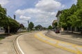 A street with cars driving, lush green trees, Louisiana Memorial Plaza, Raising CaneÃ¢â¬â¢s River Center, blue sky and clouds