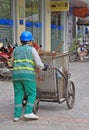 Street cleaner is wheeling trolley with garbage in