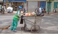 Street cleaner is wheeling trolley with garbage in