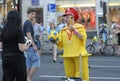 Street clown wearing yellow costume and red hat entertaining people with toy soccer balls