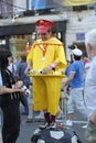 Street clown wearing yellow costume and red hat entertaining people with toy soccer balls