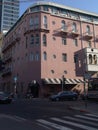 Street corner view of a crossroad and a pink four story building with parked cars