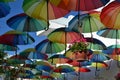 Street in Bodrum with hanging rainbow umbrellas under blue sky.